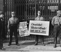 השלט השמאלי אומר: "גרמנים, הגנו על עצמכם כנגד תעמולת הזוועה היהודית. קנו רק מחנויות גרמניות!"